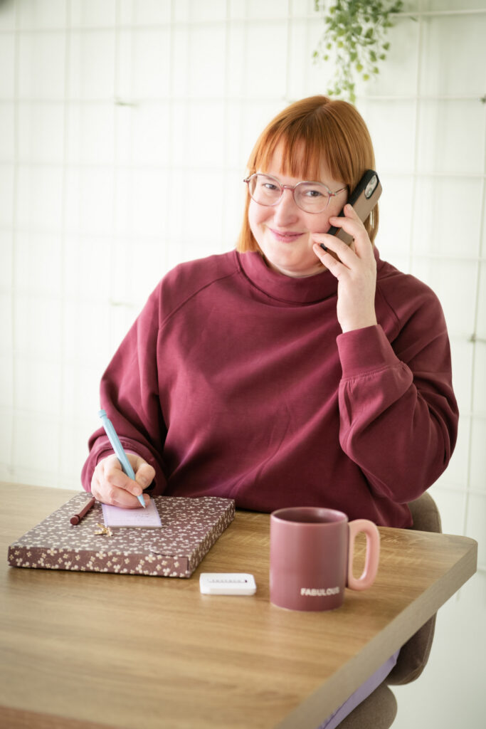 Marijke heeft de gsm in de hand en noteert terwijl ze telefoneert